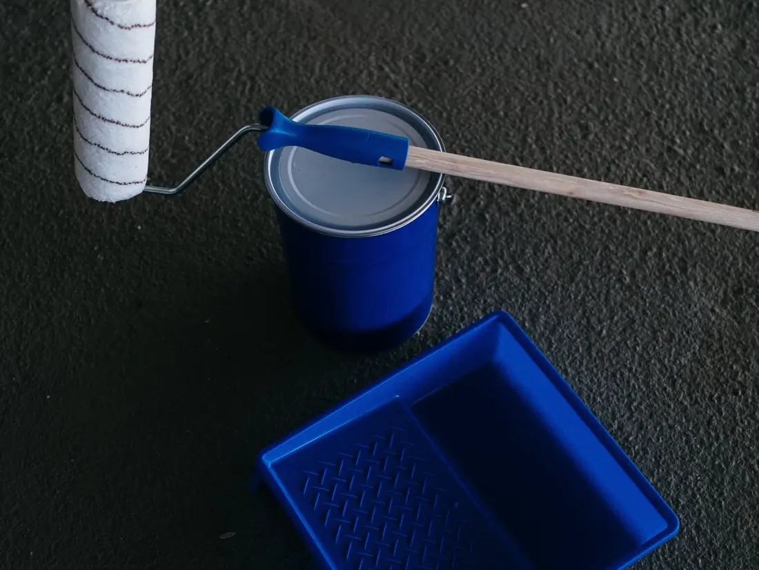 Pot de peinture, rouleau et bac posés au sol avant travaux